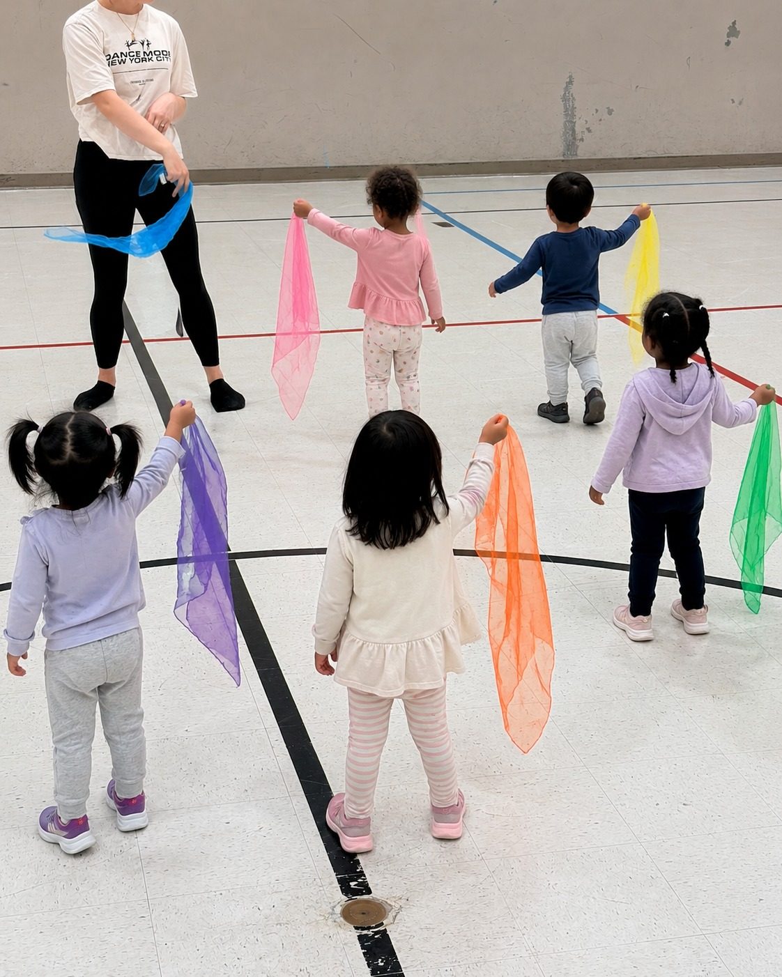 Children following an educator in a movement class, each waving a colourful scarf