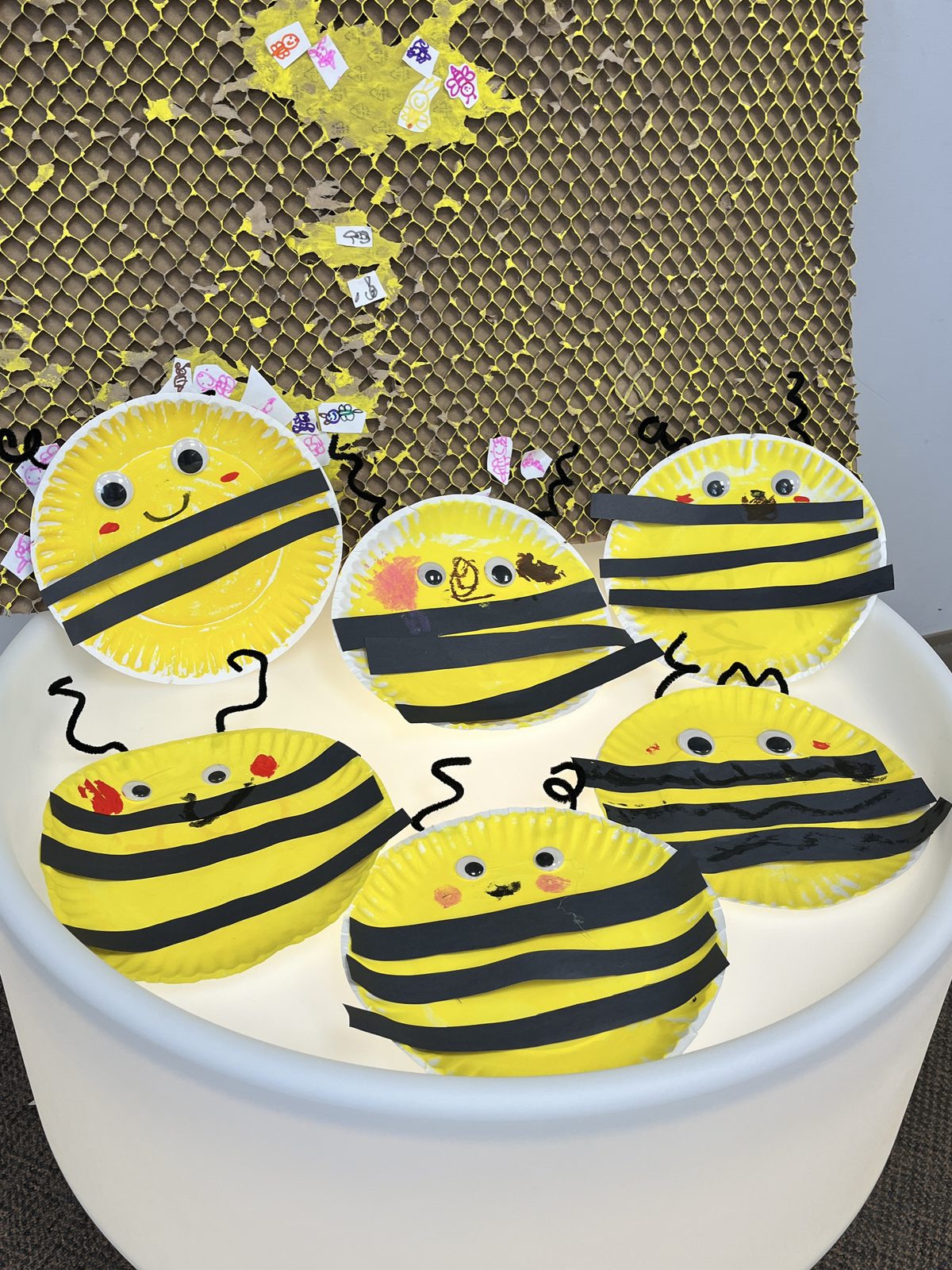 Paper-plate bees made by children displayed on a honeycomb wall
