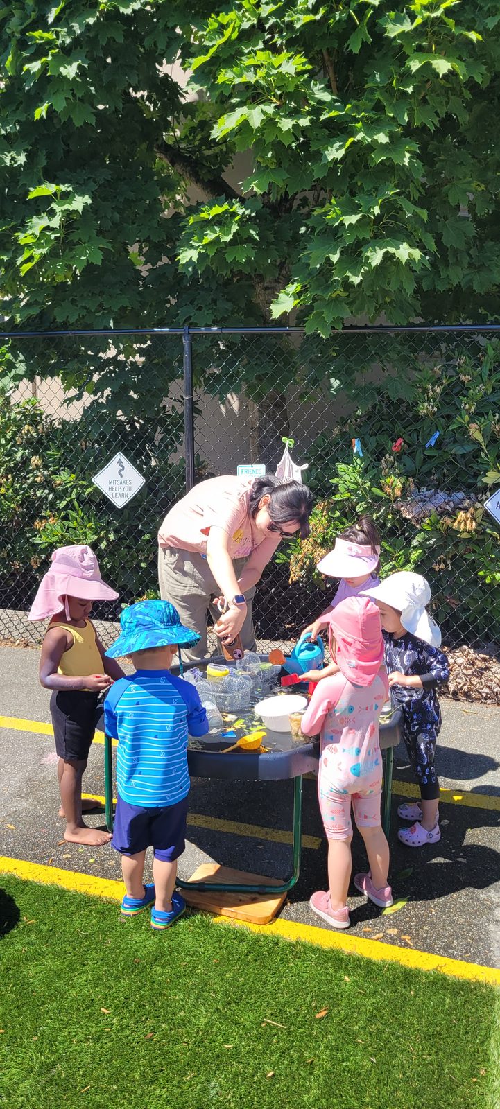 An educator working alongside children at an outdoor water table