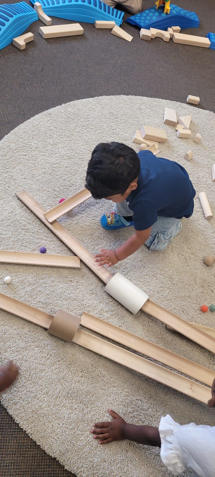 A child building a wooden marble run on the classroom rug