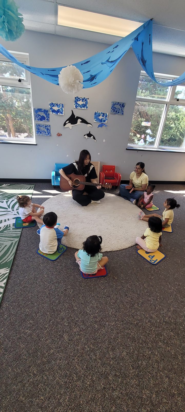 An educator playing guitar while toddlers sit in a circle during music class
