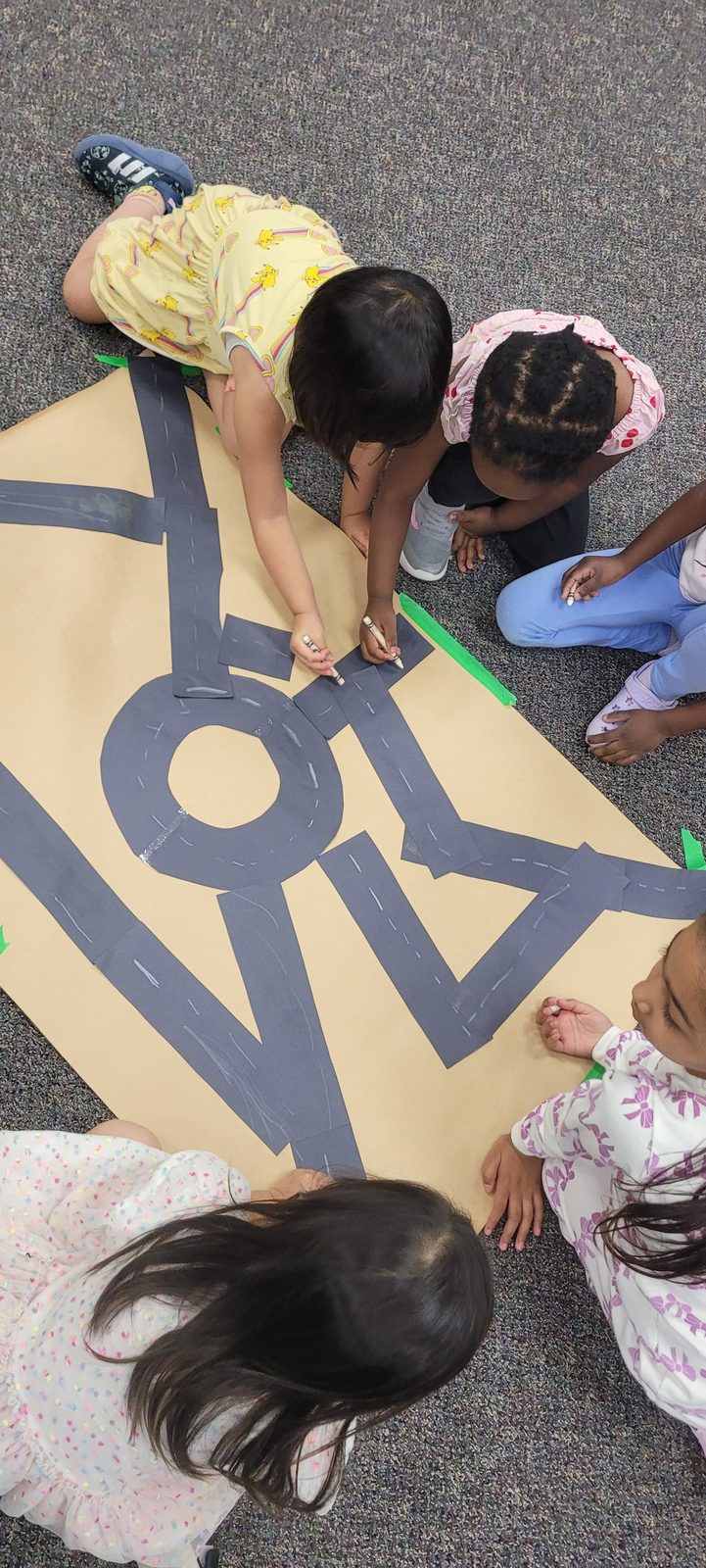 Preschoolers working together to build a paper road map across the classroom floor